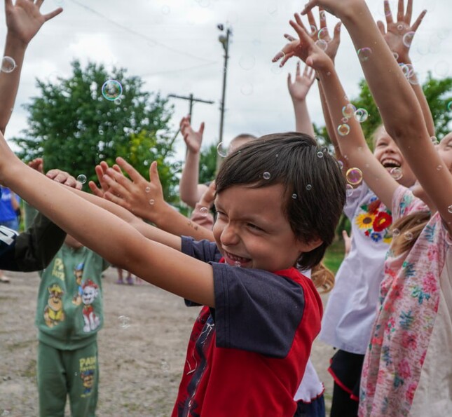 Kinder stehen im Kreis und lachen mit erhobenen Armen auf einem Platz