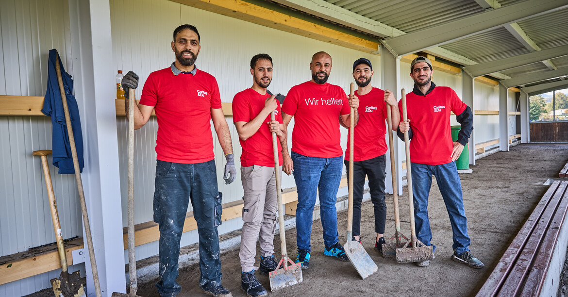 Freiwillige packten in der Hochwasserhilfe tatkräftig mit an. © Caritas / Gleiss Fünf Freiwillige mit Werkzeug in roten Caritas-Shirts bei Aufräumarbeiten nach einem Hochwasser