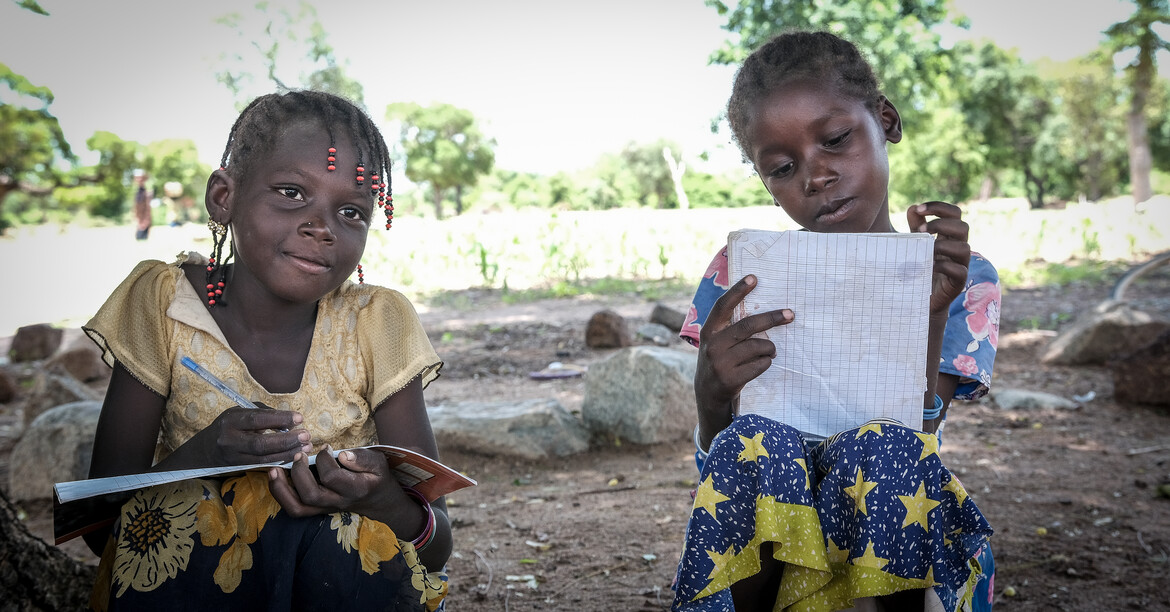 Die Hilfe der Caritas in Burkina Faso setzt ganzheitlich an: Von der Nothilfe bis hin zu nachhaltiger Unterstützung, die Perspektive schafft. © Caritas / Drabo Zwei Mädchen sitzen draußen und schreiben in Schulhefte