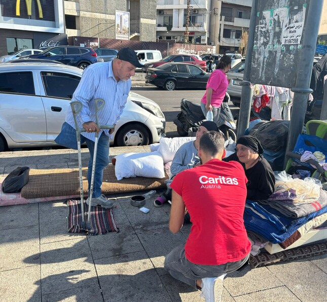 Caritas Mitarbeiter*innen im Gespräch mit Person auf Bank im öffentlichen Raum