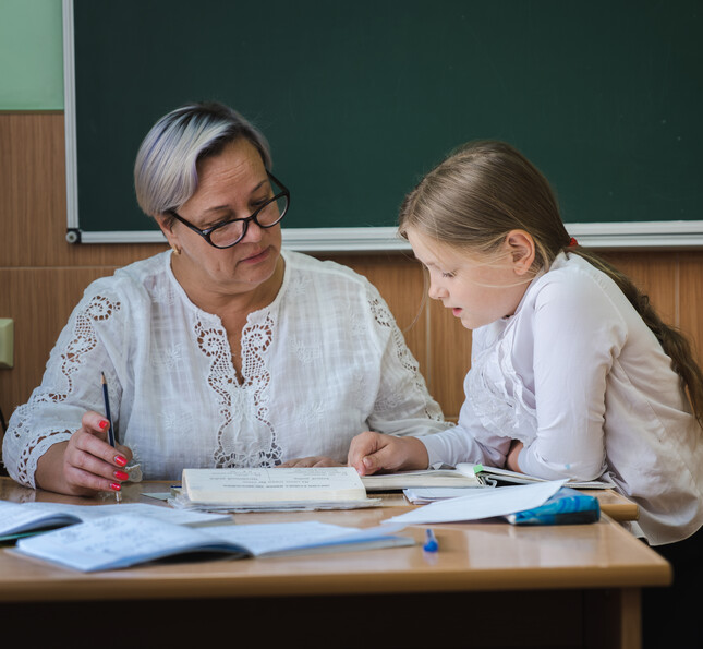 Ältere Lehrkraft erklärt Schulstoff einem Mädchen im Klassenzimmer
