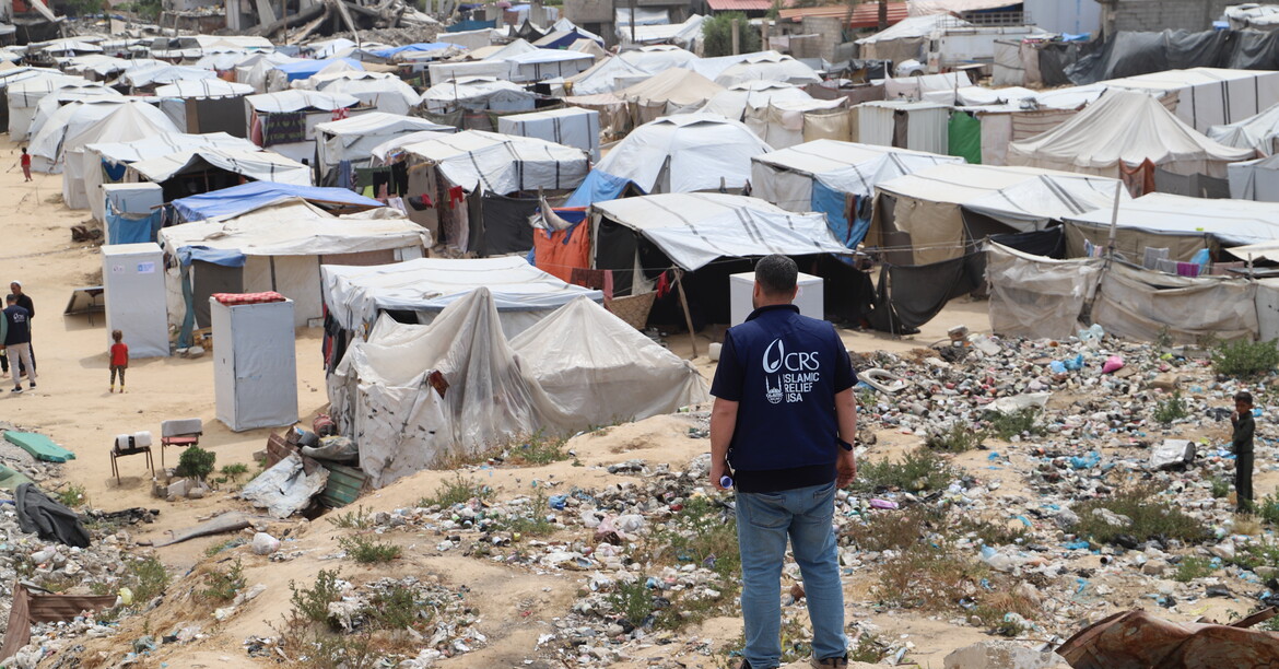 Eine Person mit Caritas-Weste blickt auf ein dichtes Zeltlager im Krisengebiet Gaza.