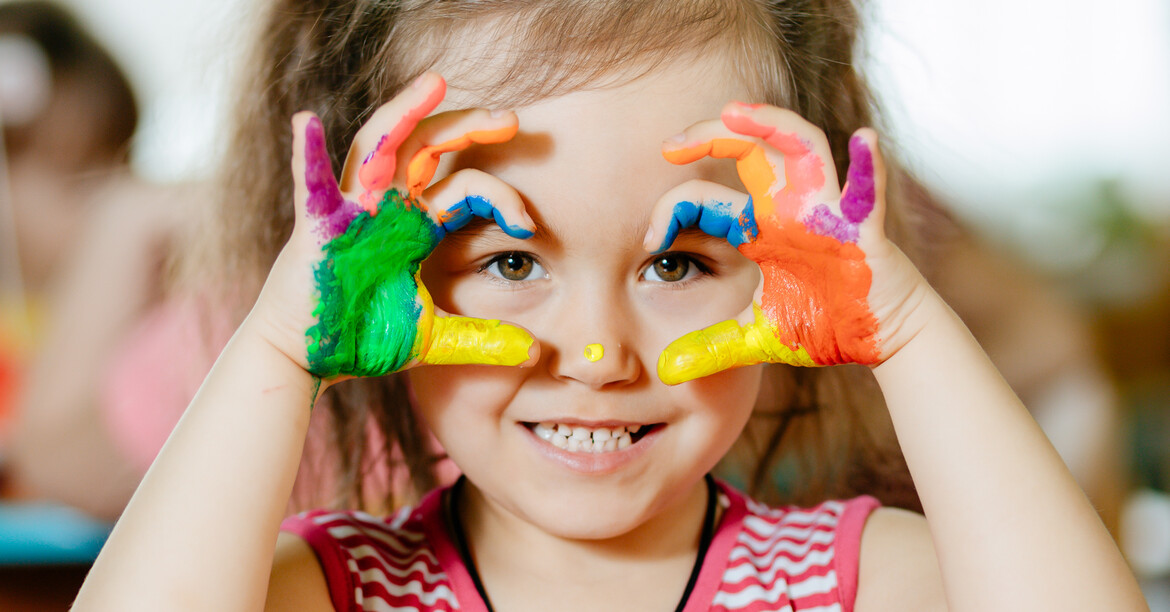 Mädchen im Kindergarten-Alter spielt mit bunten Bausteinen und lächelt durch Spielgerät