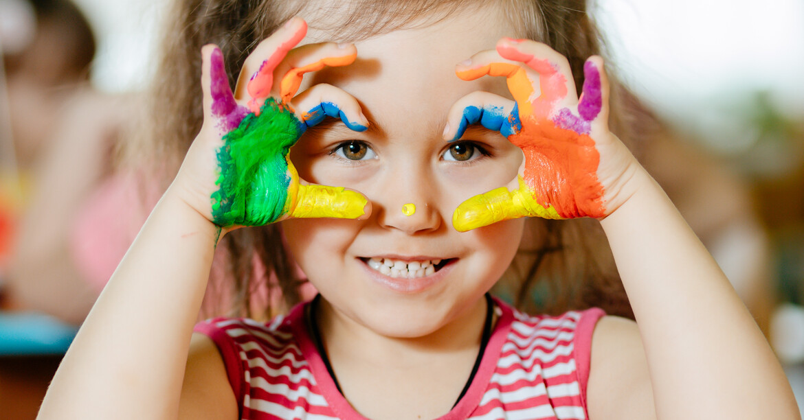 Mädchen im Kindergarten-Alter spielt mit bunten Bausteinen und lächelt durch Spielgerät
