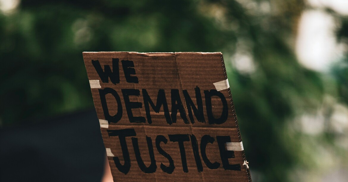 Person hält Schild mit Aufschrift „We demand justice and change“ hoch