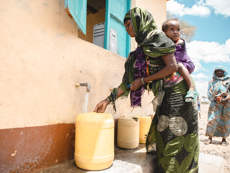 Eine Frau in afrikanischem Gewand füllt einen Kanister mit Wasser